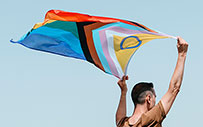 A person waves an multicolored, inclusive flag.